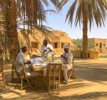 Three men at table under palm trees