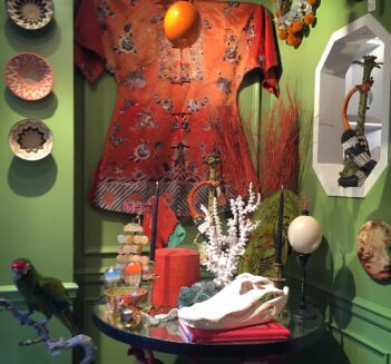 Interior with green wall, woven baskets, red silk kimono, table with mounted coral, alligator skull, mounted ostrich egg, and glass jellyfish