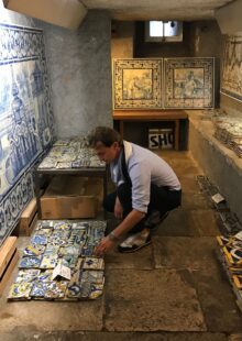 Marco kneeling down looking at blue and white tile in tile shop lined with tile on wall.  
