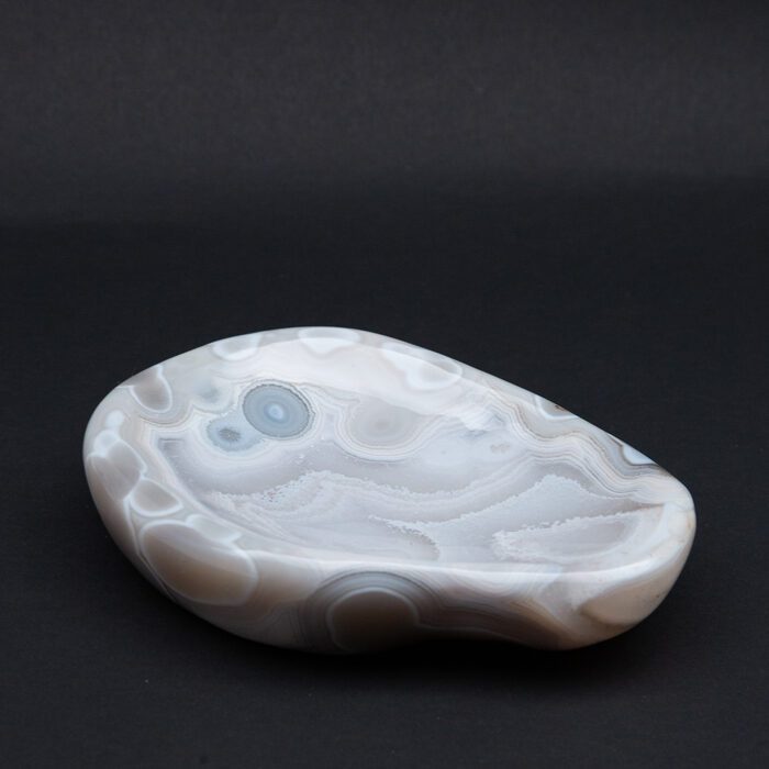 Agate vide poche with bands of light blue, white, brown, with amorphous shape. Resting on black background